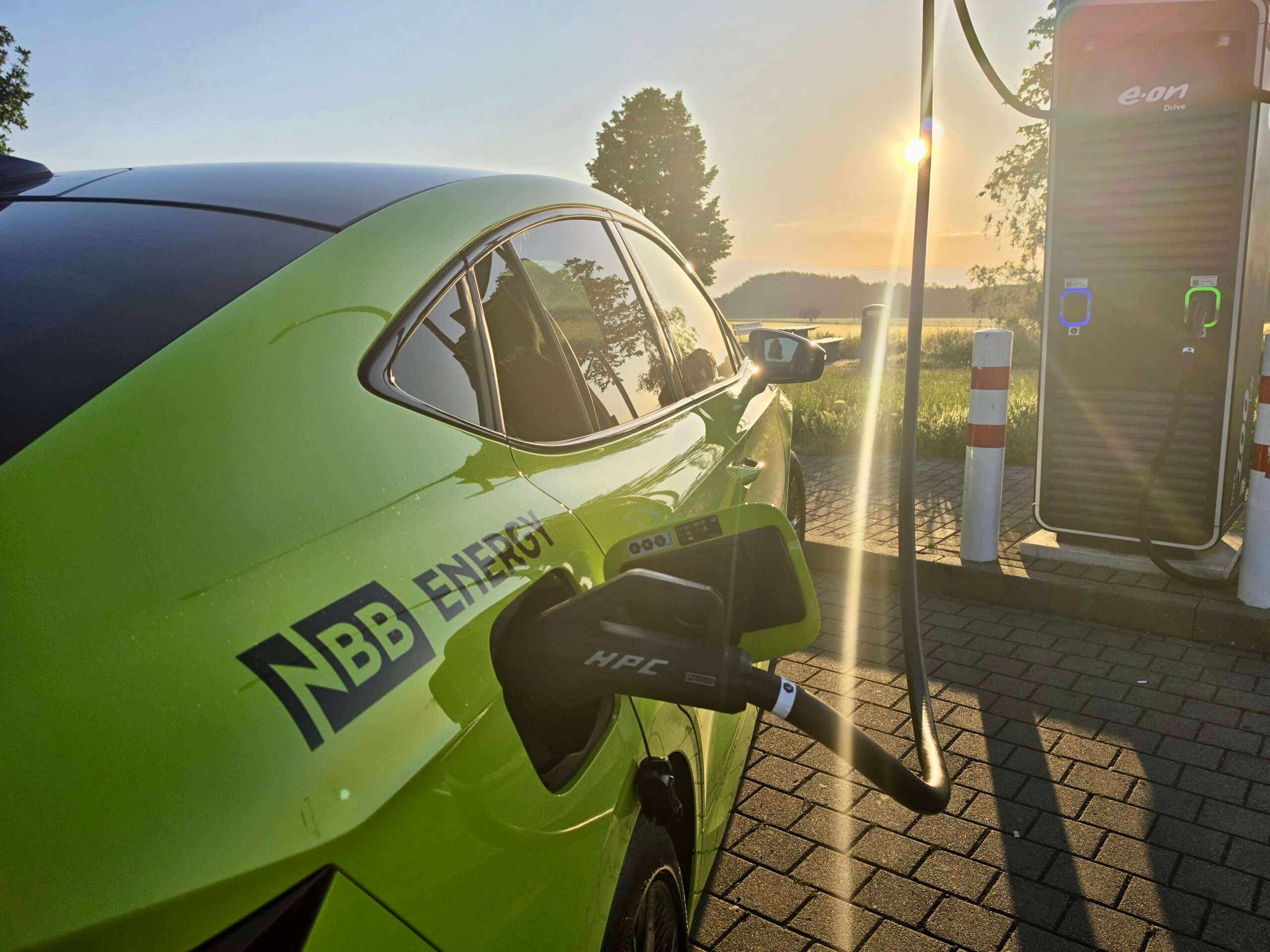 NBB ENERGY Auto lädt an E-Ladesäule bei Sonnenuntergang