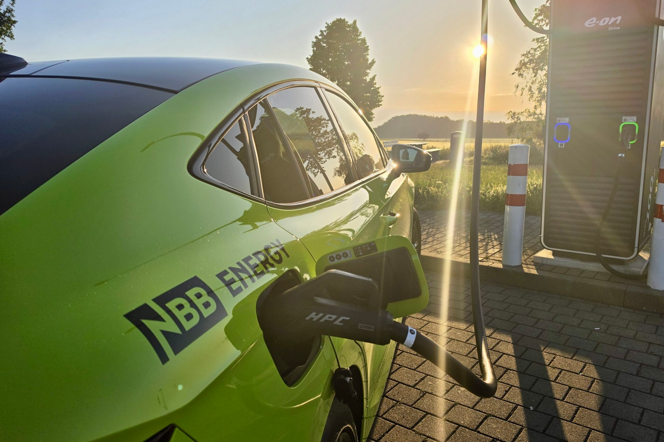 NBB ENERGY Auto lädt an E-Ladesäule bei Sonnenuntergang